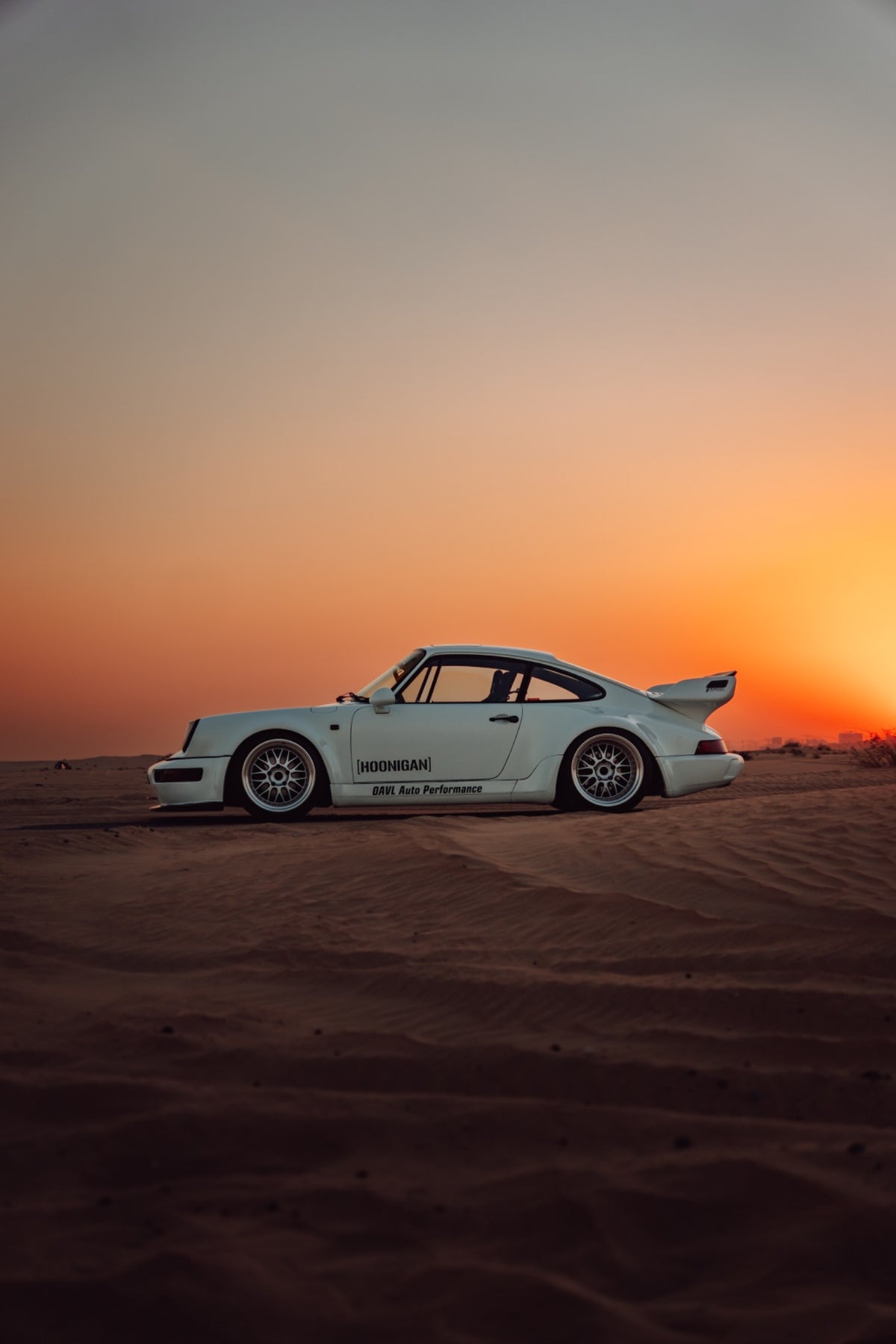 White Porsche 911 photographed against a warm sunset over sandy terrain
